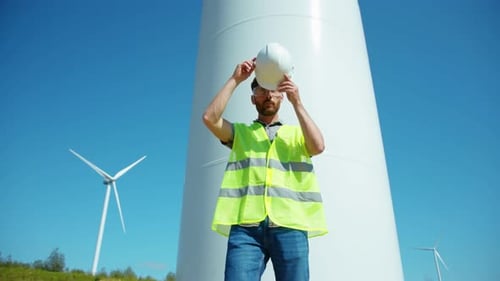 Young Man Engineer in Uniform Puts on a Helmet Stand Near Wind Turbines Ecological Energy Industry