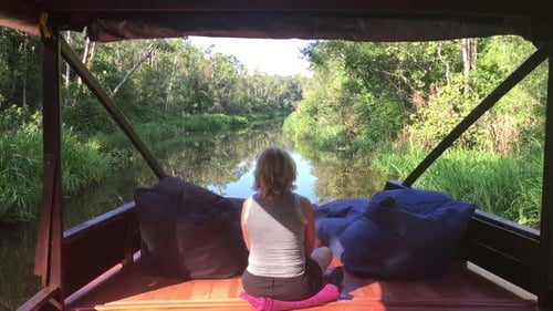 Woman Meditating on Riverboat in Peaceful Jungle Setting