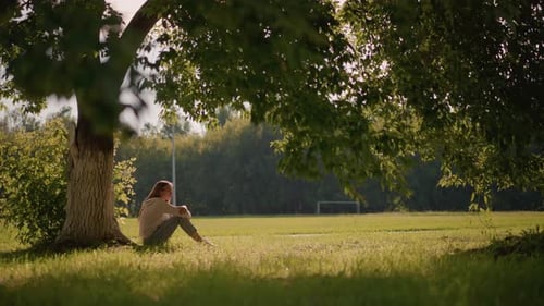 Thoughtful Woman Seated Under Tree in Peaceful Park