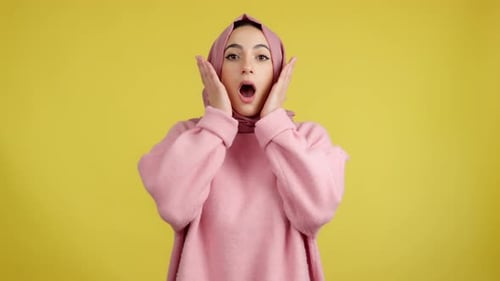 Surprised Woman in Pink Headscarf Against Yellow Background