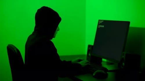 Hacker with a white mask turning his face towards the camera in a dimly lit room. Medium shot
