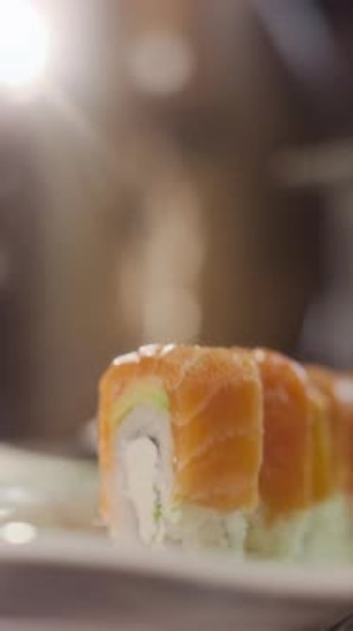 Close Up Man Putting Salmon Sushi Roll on Plate Vertical