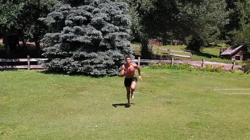 Young caucasian fit attractive male sprinter running exercising outdoors with green vegetation back