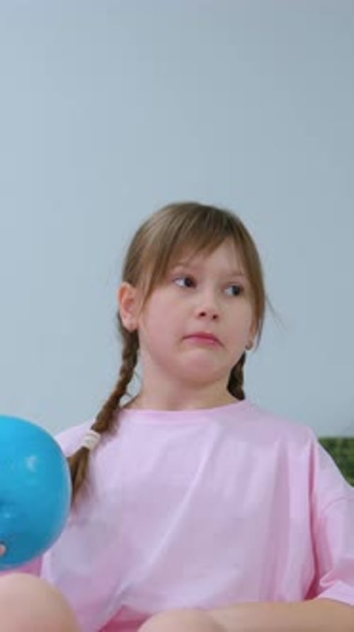Child in Pink Balancing on Blue Stability Ball Holding Balloon in Gym Setting