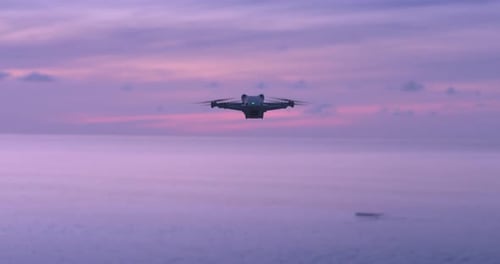 Modern Drone Hovered in the Air Drone Quad Copter on Sea Background at Beautiful Pink Sunset Travel