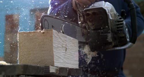 Close-up of chainsaw cutting through wooden plank, wood chips and shavings scattering in super slow