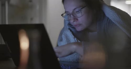 Tired woman with glasses studying late night in front of laptop, static view