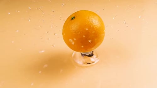 Super Slow Motion Shot of Flying Fresh Orange Slices and Water Side Splash on Orange Background