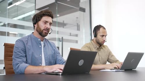Two Men Working at Desks with Headsets and Laptops