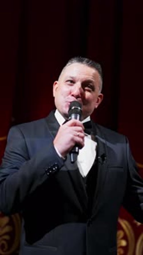 Man in Tuxedo Speaking into Microphone on Stage