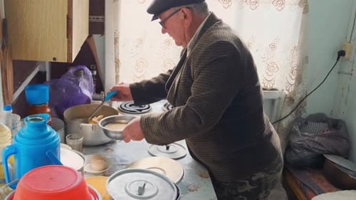 Senior Man Ladling Soup at Home in Kitchen