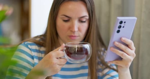 Woman Uses Phone While Drinking a Beverage