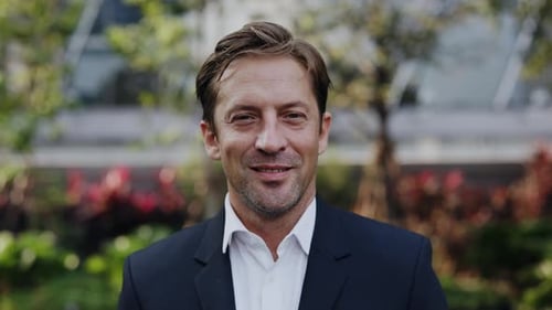 Portrait of Businessman in Formal Suit Looks at Camera Standing in Urban Park