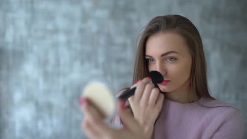 Woman Applying Makeup with Brush in an Indoor Setting