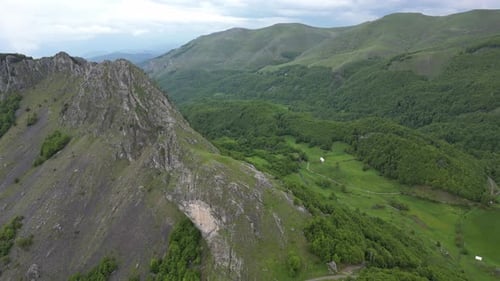 Flying over beautiful green mountains. In the background, stone cliffs with snow are visible.