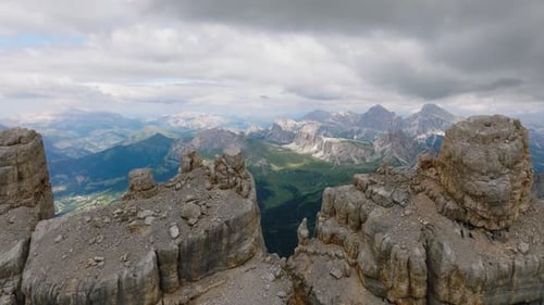 Aerial trucking shot of rocky peaks of mountain and green valley - tilt down flight - CLoudy sky in