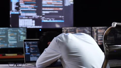 Vue arrière d'un programmeur asiatique endormi en écrivant du code par un ordinateur portable utilisant plusieurs moniteurs