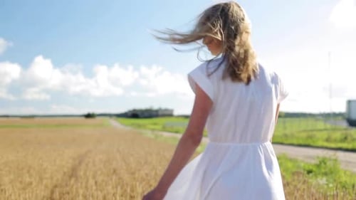 Carefree young woman in white dress dancing and spinning in a sunny wheat field