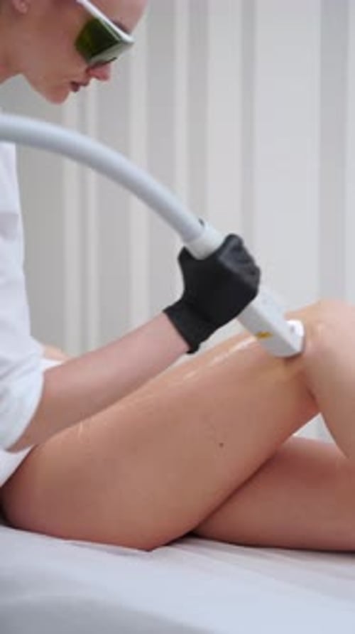 Skincare Specialist Performs Laser Hair Removal on Clients Leg in Clinic Room Patient Lies for