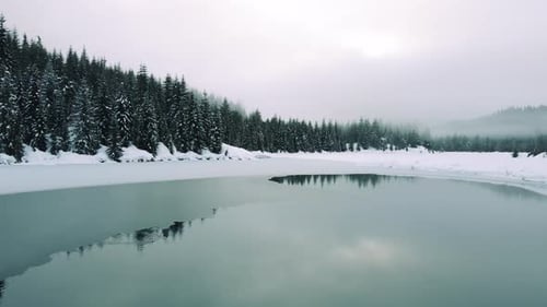 Drone Dolly Over Calm Lake Water Reflecting Breathtaking Forest Trees In Hazy Winter Fog