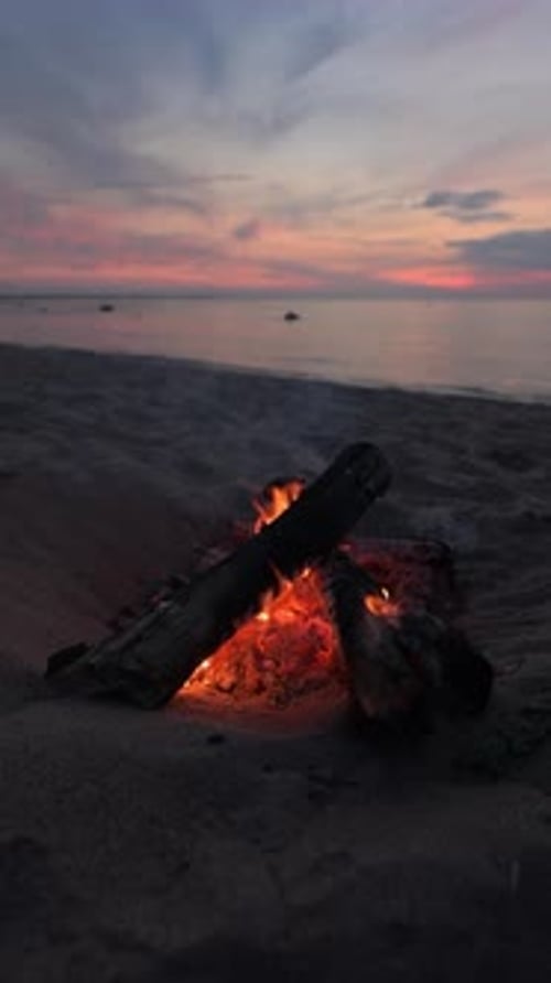 Lagerfeuer an einem Sandstrand bei Sonnenuntergang.