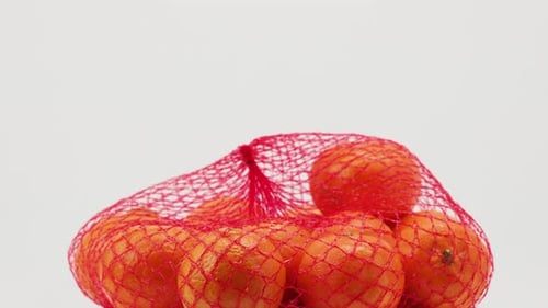 A group of tropical tangerine fruits in a mesh package rotate on a white background.