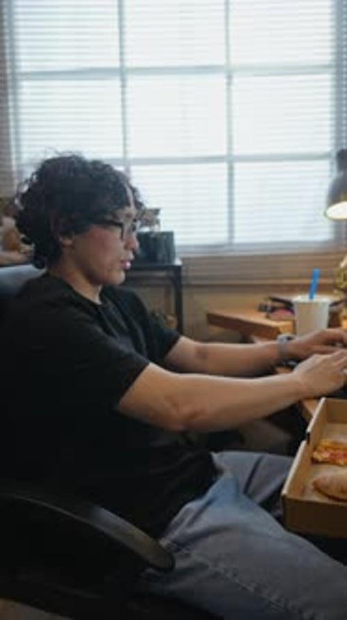 Asian Man Eating Pizza and Using Smartphone at Home Office