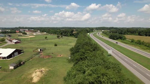 An aerial view of a curved road next to an open field with a line of trees separating them. There ar