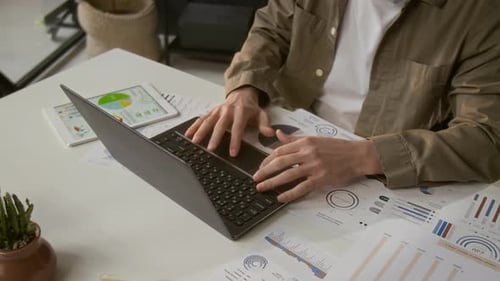 Typing on Laptop Surrounded by Charts