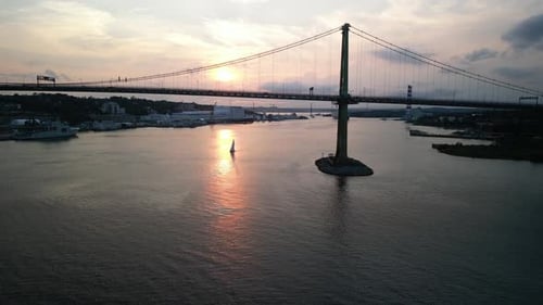 Drone filmé au cinéma : un voilier navigue sous un pont suspendu au coucher du soleil