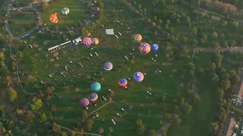 Rotating aerial view of hot air balloons taking off from a park.