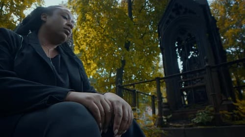 Grieving Woman Sitting in Cemetery and Contemplating Grave