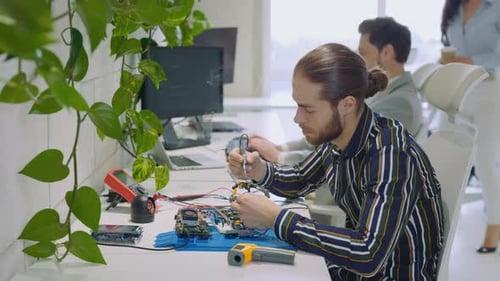 Männlicher kaukasischer Ingenieur im Labor sitzt am Schreibtisch, Lötkolben, Leiterplatte