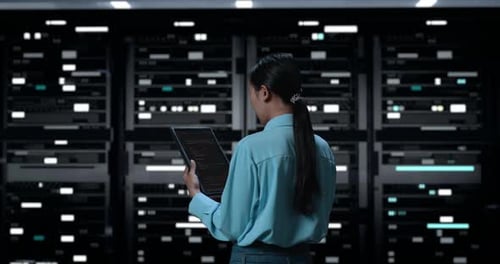Back View Of A Woman Looking At Database On Terminal Window Showing On Digital Tablet In Dark Server
