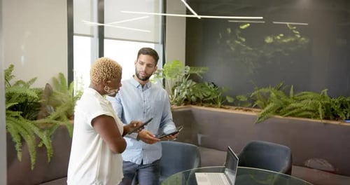 Discussing work, multiracial colleagues using tablets and laptop in modern office setting