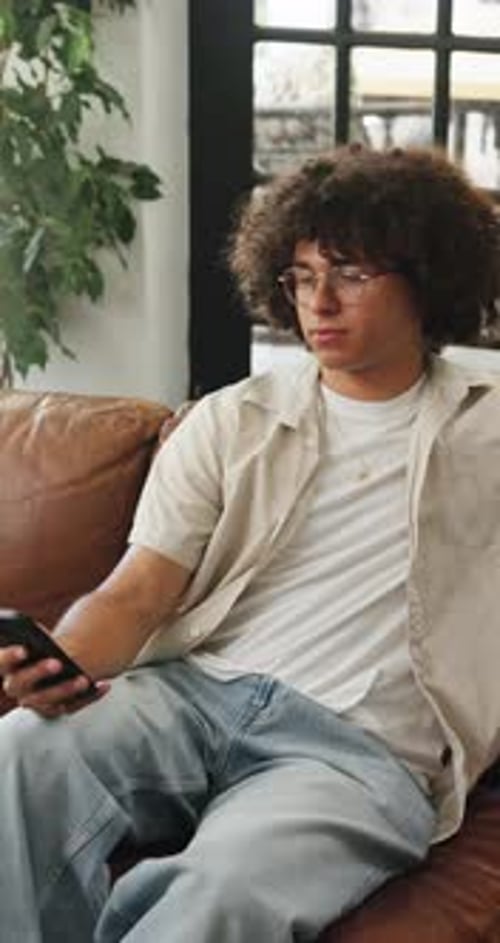 Young Man Using Smartphone Sitting on Couch at Home
