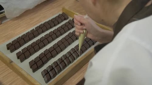 pastry chef decorating square chocolates with white garnish