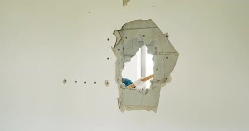 Closeup of a Hole in a Wall Where a Man is Hitting It with a Hammer