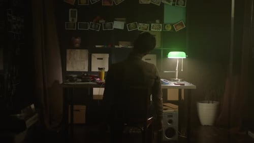 Person Sitting at Desk in Dark Room Under Green Lamp Light