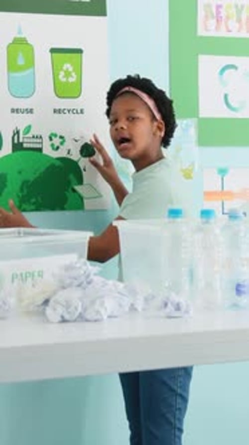 Vertical video: Starting student presenting recycling in classroom, sorting paper into PAPER bin