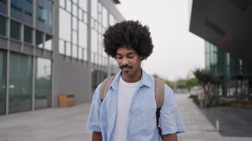Joven afroamericano seguro de sí mismo caminando en la ciudad y sonriendo mirando a la cámara