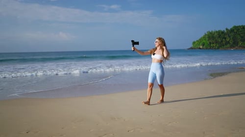 Fashionable Female Vlogger Records Content with Gimbal Stabilized Camera at Beach Blonde Influence