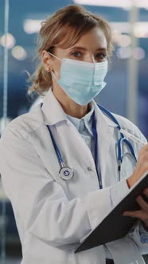 Female Doctor Writing on Clipboard with Face Mask