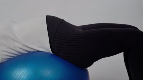 A Pregnant Woman Strengthens Her Abdominal Muscles with a Fitball While Lying on Her Back on a White