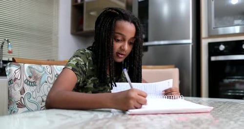 Teen Girl Writing in Notebook at Kitchen Table