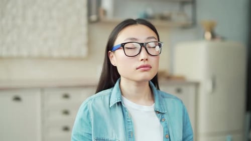 Close-up of a young asian woman meditating with her eyes closed while sitting in the living room.