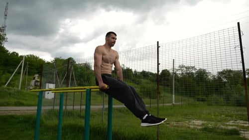 Muscular Man Exercising on Parallel Bars Outdoors