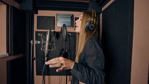 girl singer singing in a recording studio with headphones in front of microphone to create a song