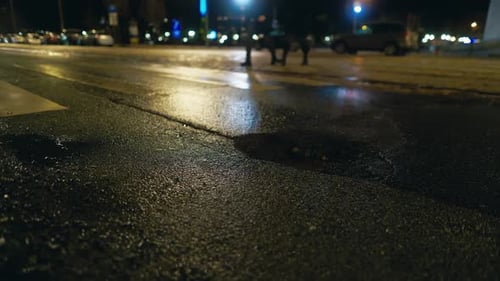 Cena noturna de pessoas atravessando a estrada de asfalto sob luzes de rua fracas