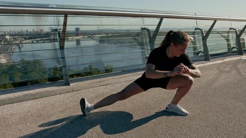 Fitness young sportswoman girl in the morning doing warm-up leg exercises before training on street